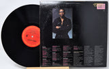 A vinyl record partially pulled from its black album cover, showing the back of the package with a portrait photo and track listings. The record label has a bright orange-red center label.