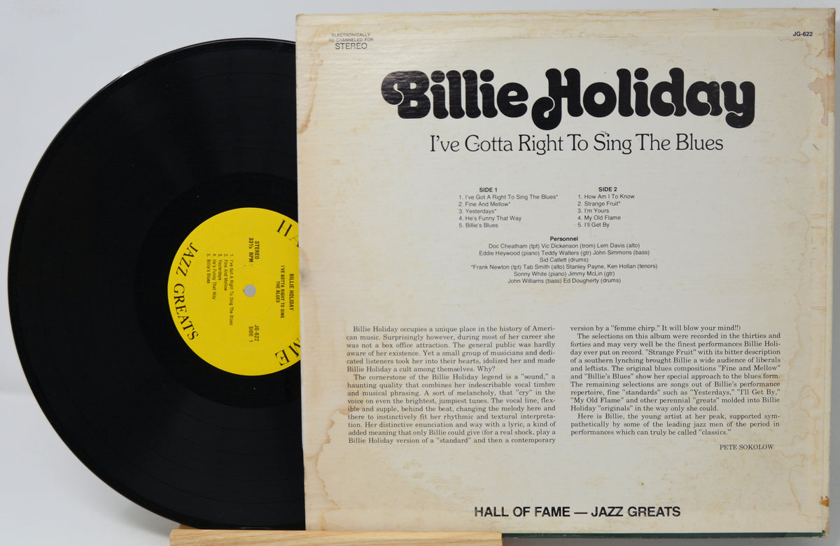 A vintage Billie Holiday vinyl record partially pulled from its cream-colored sleeve, showing the black record with a yellow label and the back cover text.