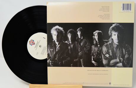 A vinyl record partially pulled from its sleeve, showing the black record and the cream-colored back cover with a black-and-white band photo and track listing.