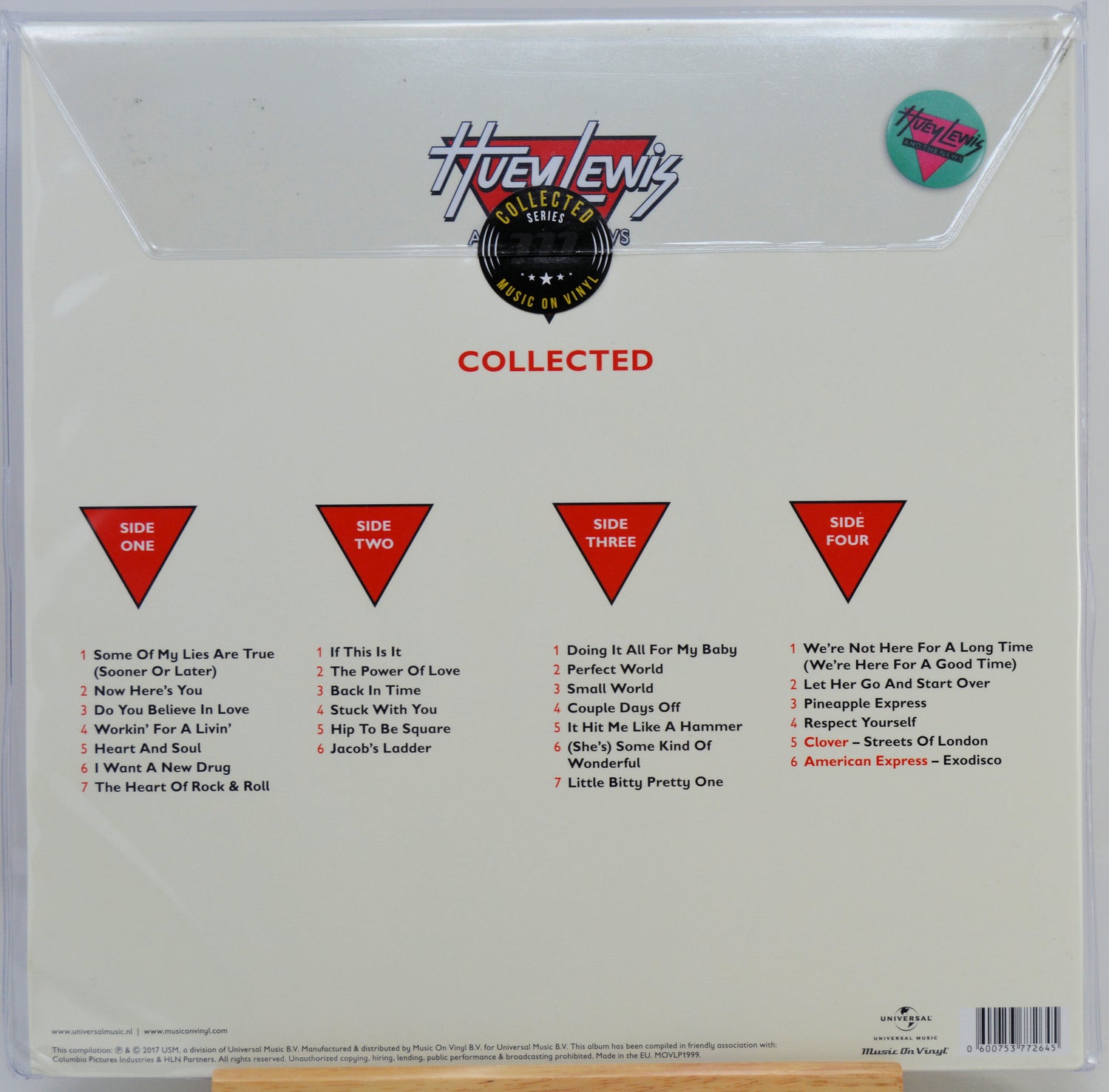 The back cover of a vinyl record album in a clear plastic shrink wrap, featuring the Huewenz 'Collected' compilation. The cover is off-white with red and black text, listing track selections for four sides, and includes a circular sticker.