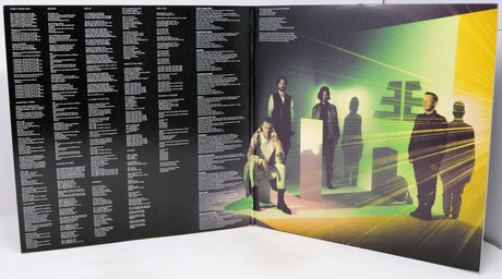 Vinyl record with a black cover featuring text on the left and a colorful album cover on the right with people in a room.