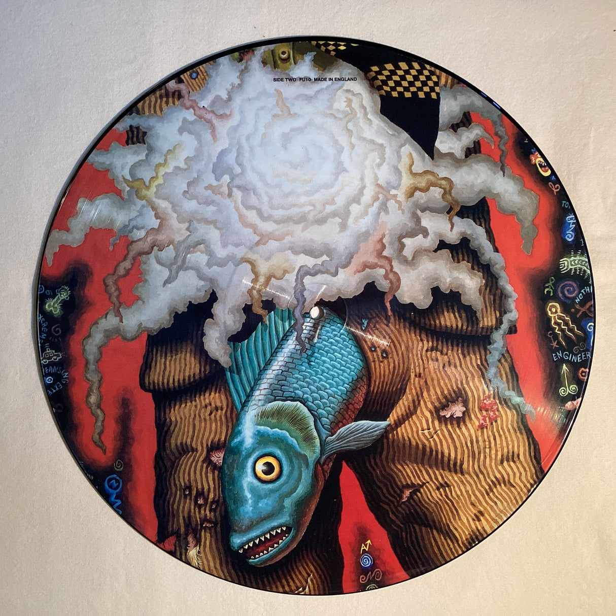 Surreal picture disc with a blue fish and abstract clouds on vivid red background