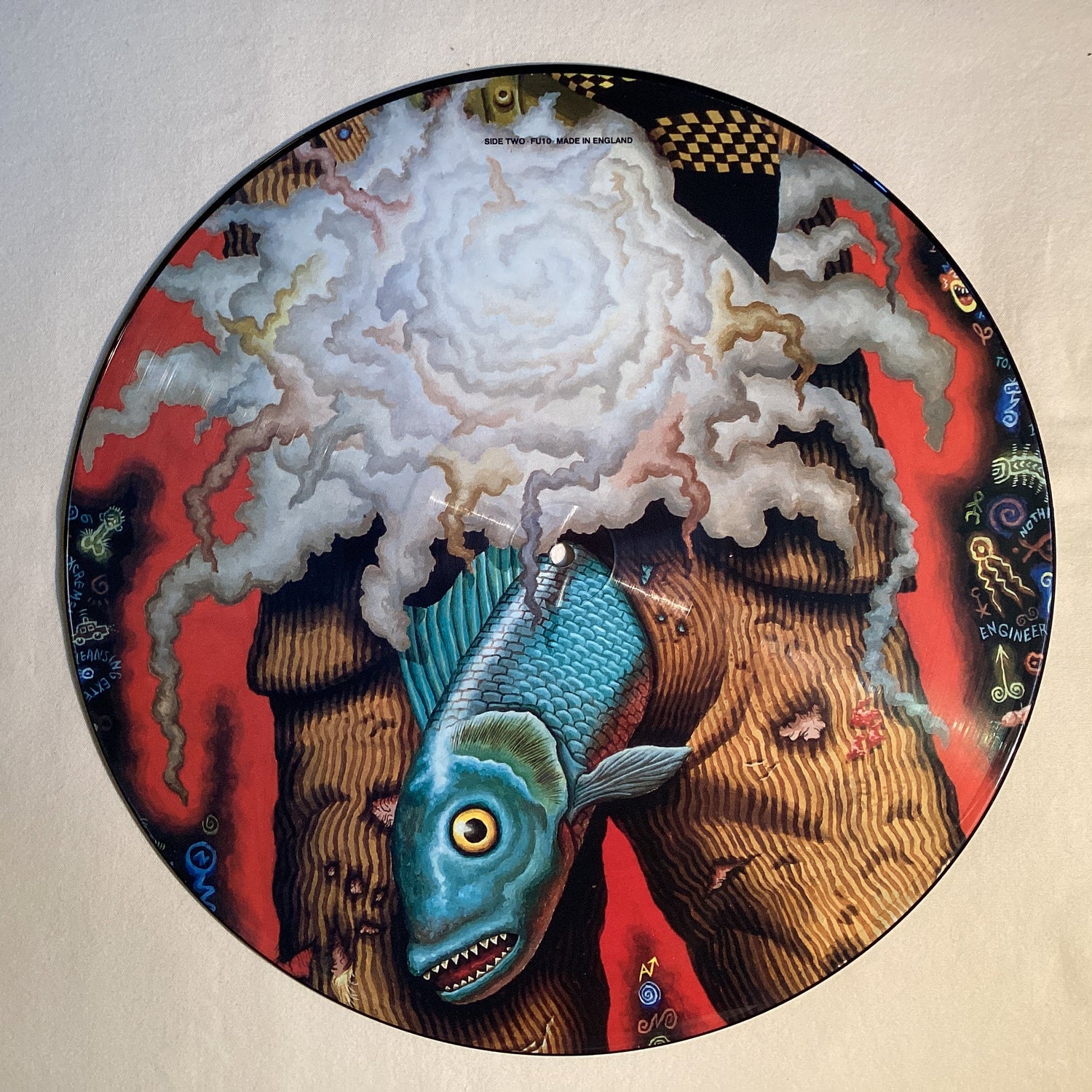 Surreal picture disc with a blue fish and abstract clouds on vivid red background