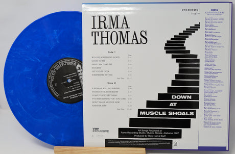A blue translucent vinyl record partially tucked behind its printed album cover for Irma Thomas's 'Down at Muscle Shoals.' The cover shows black text and staircase graphics on a white background, with the Chixx / Gress label branding visible.