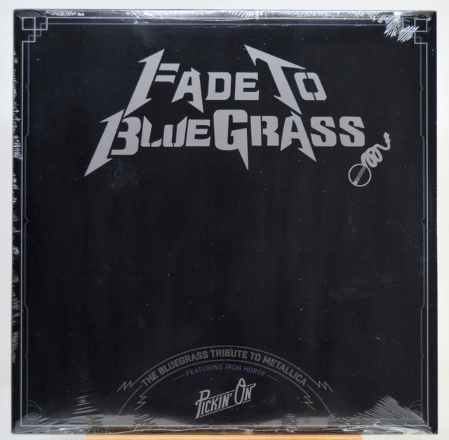 A square black album cover for 'Fade To Blue Grass' wrapped in clear plastic, featuring a white stylized logo and text, photographed against a white background.