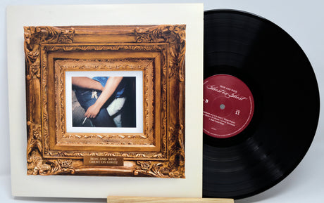 A vinyl record partially pulled from its sleeve, showing the ornate gold-toned album cover art and a black record with a red center label on a light gray background.