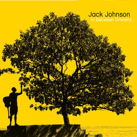 An album cover featuring a silhouette of a person standing next to a large tree with a yellow background, representing the artist Jack Johnson and the album 'In Between Dreams'.