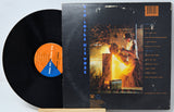 A vinyl record partially pulled from its sleeve, showing the black record, orange and blue center label, and the back cover artwork with a fiery welding scene and track listing.
