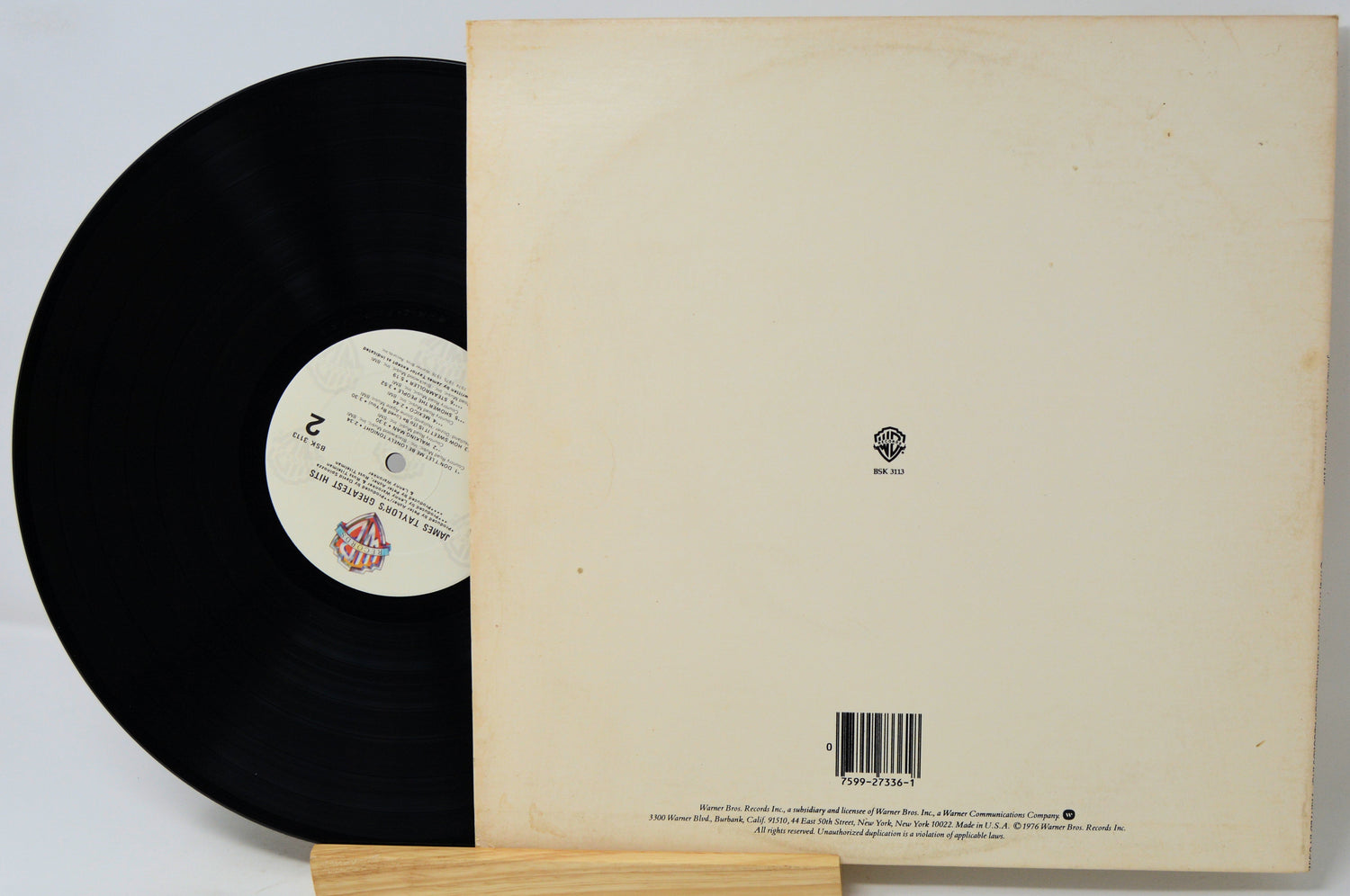 A vinyl record partially pulled from its cream-colored paper sleeve, displayed on a small wooden stand against a white background.