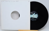 A black vinyl record partially pulled from a white sleeve with a circular cutout, displayed on a small wooden stand against a light gray background. The center label shows the text 'Jean Spirit'.