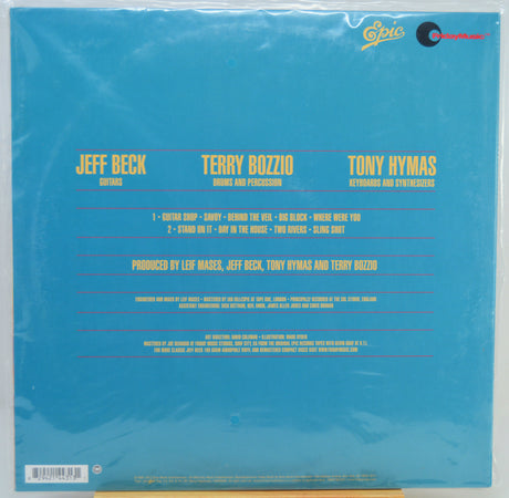 The back cover of a vinyl record sleeve for Jeff Beck and Terry Bozzio's 'Guitar Shop' on Epic Records, featuring a bright blue background with yellow text and a glossy plastic wrap.
