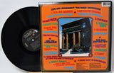 Vinyl record with its cover featuring text and a building image on an orange background.