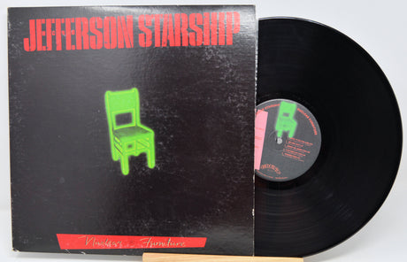 Jefferson Starship vinyl record album with the black LP partially pulled from the sleeve. The sleeve is black with bold red 'JEFFERSON STARSHIP' text and a bright green chair graphic, photographed against a light neutral background.