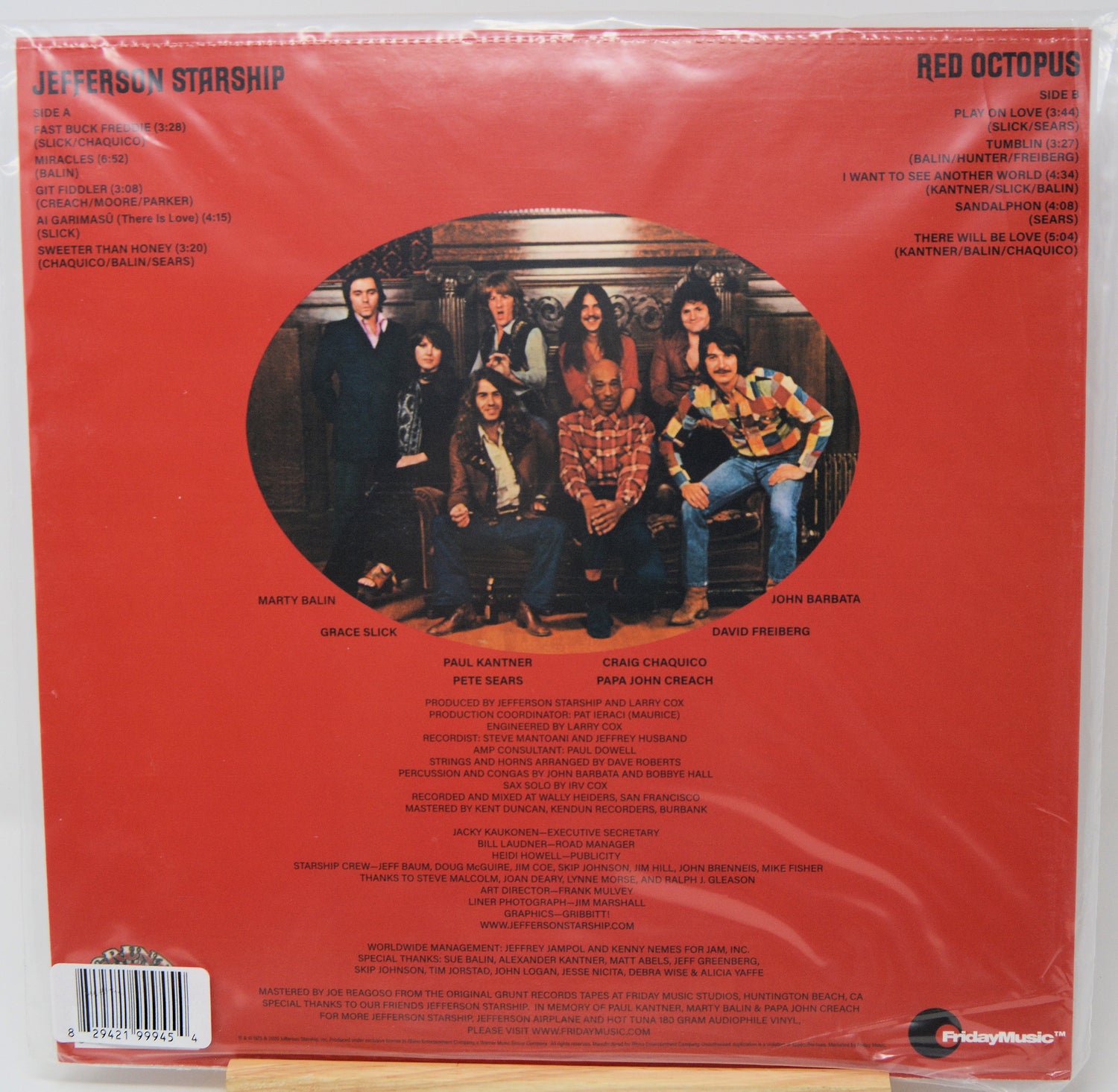 The back cover of the Red Octopus vinyl record album by The Jefferson Starship, sealed in its plastic shrink wrap. The cover features a solid red background with a large circular photo of the band members in the center, track listings on the top and bottom, and a barcode in the lower-left corner.