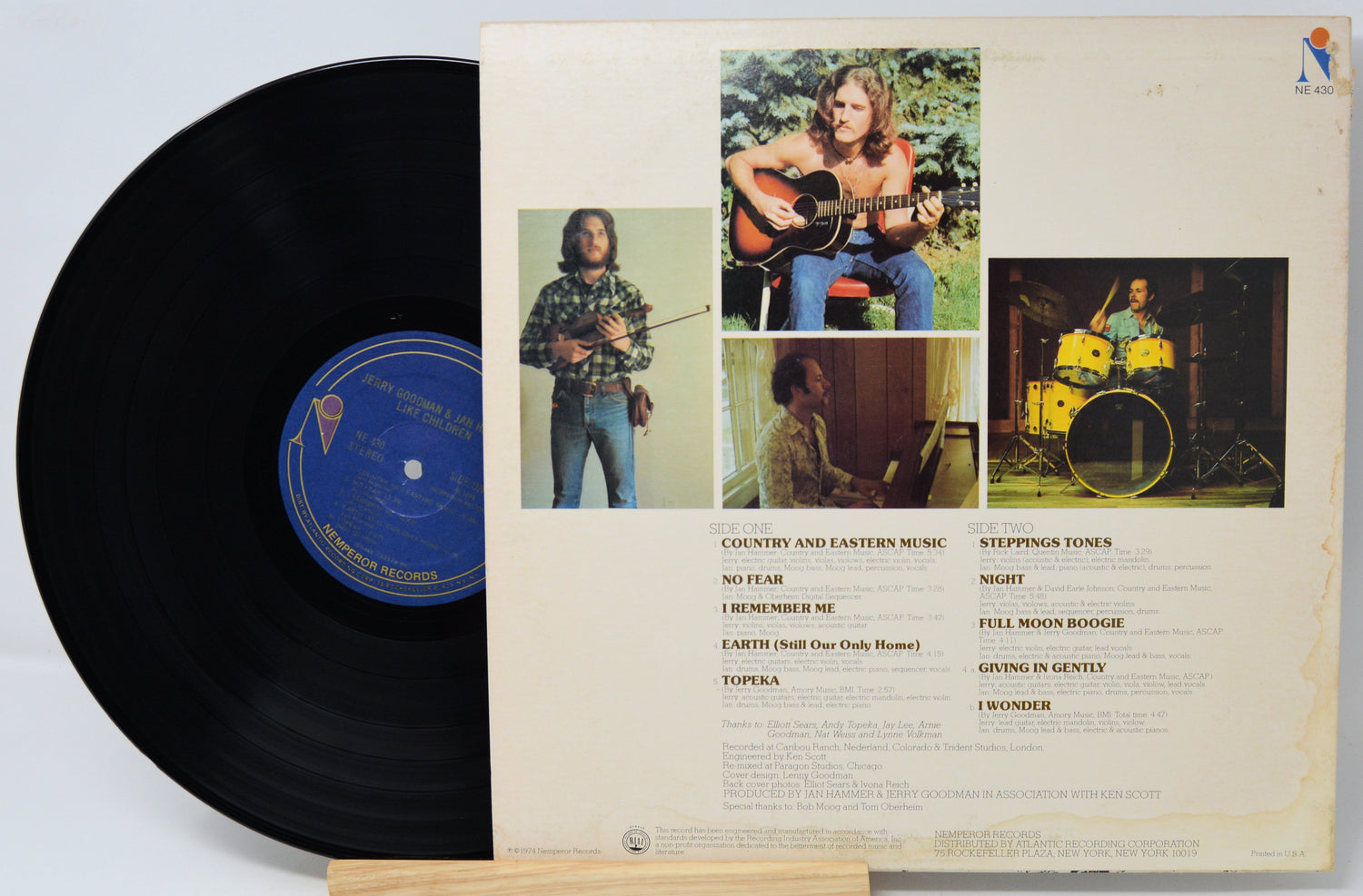 A vinyl record partially pulled from its back cover sleeve, showing the black record on the left and the cream-colored printed back cover on the right with three photos of a musician and track listings.