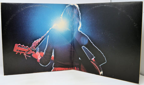 A vintage vinyl record sleeve or album cover displayed open, featuring a silhouetted figure playing an electric guitar against a dark background with a bright spotlight effect.