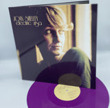 Vinyl record with a purple disc and cover featuring a person's face, on a light gray background.