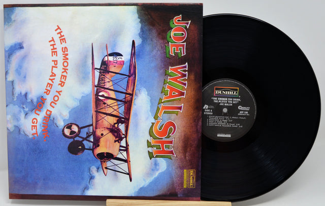Joe Walsh 'The Smoker You Drink' vinyl record shown with its illustrated album cover and the black record partially pulled out, photographed on a light gray background.