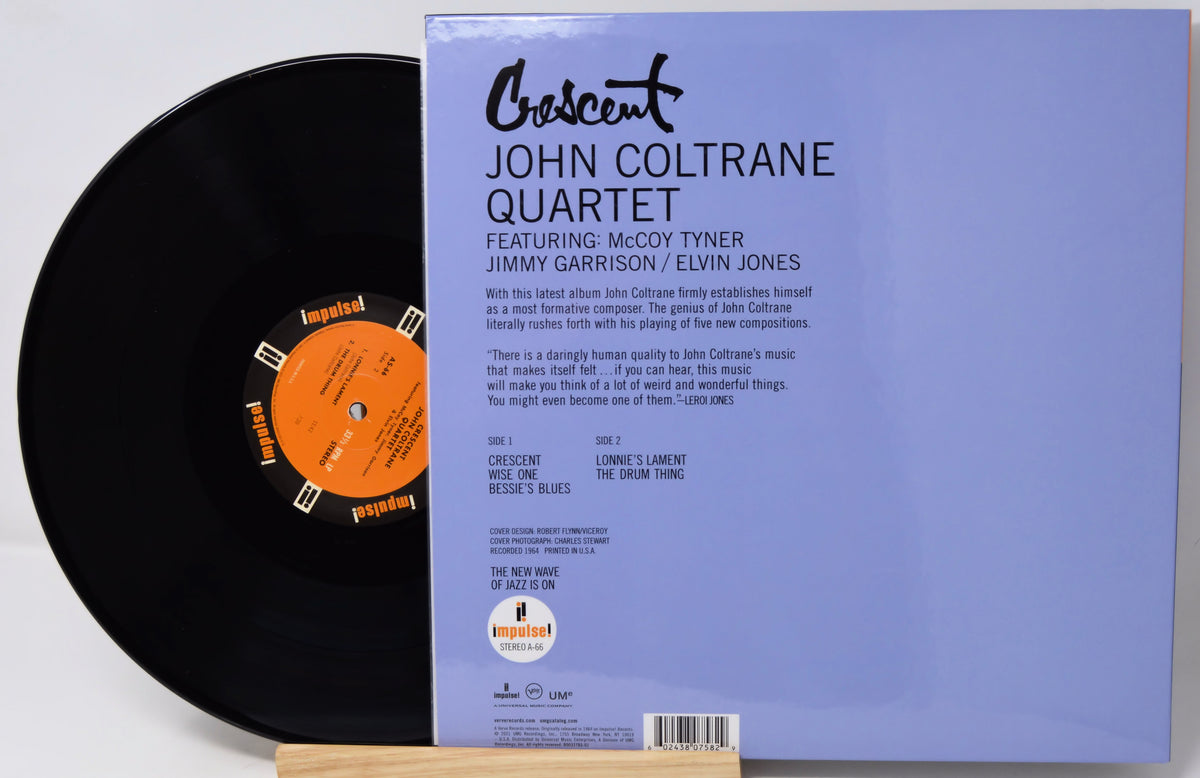 Vinyl record album cover and part of the black record sleeve displayed on a wooden stand. The cover reads 'Crescent John Coltrane Quartet' with track listing and artist names, and the record label 'Impulse!' is visible on the orange label and lower left.