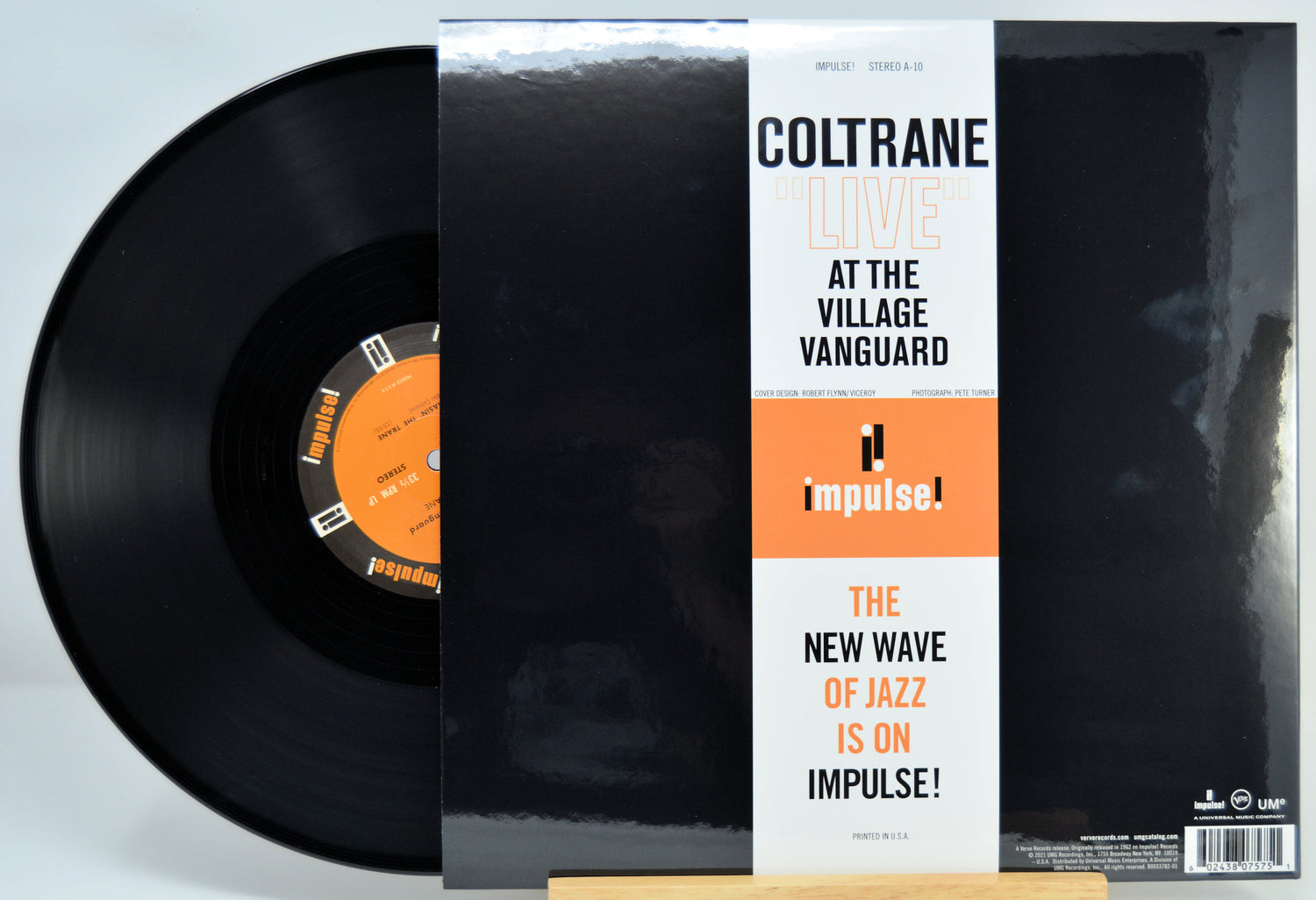 A vinyl record partially pulled from its sleeve, showing the black record and the cover art for Coltrane's 'At the Village Vanguard' on Impulse Records.