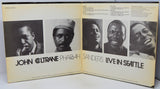 An open vinyl record album showing the inner cover artwork for 'John Coltrane Pharaoh Sanders Live in Seattle', featuring black-and-white portrait photos of the musicians and cream-colored paper with printed text.
