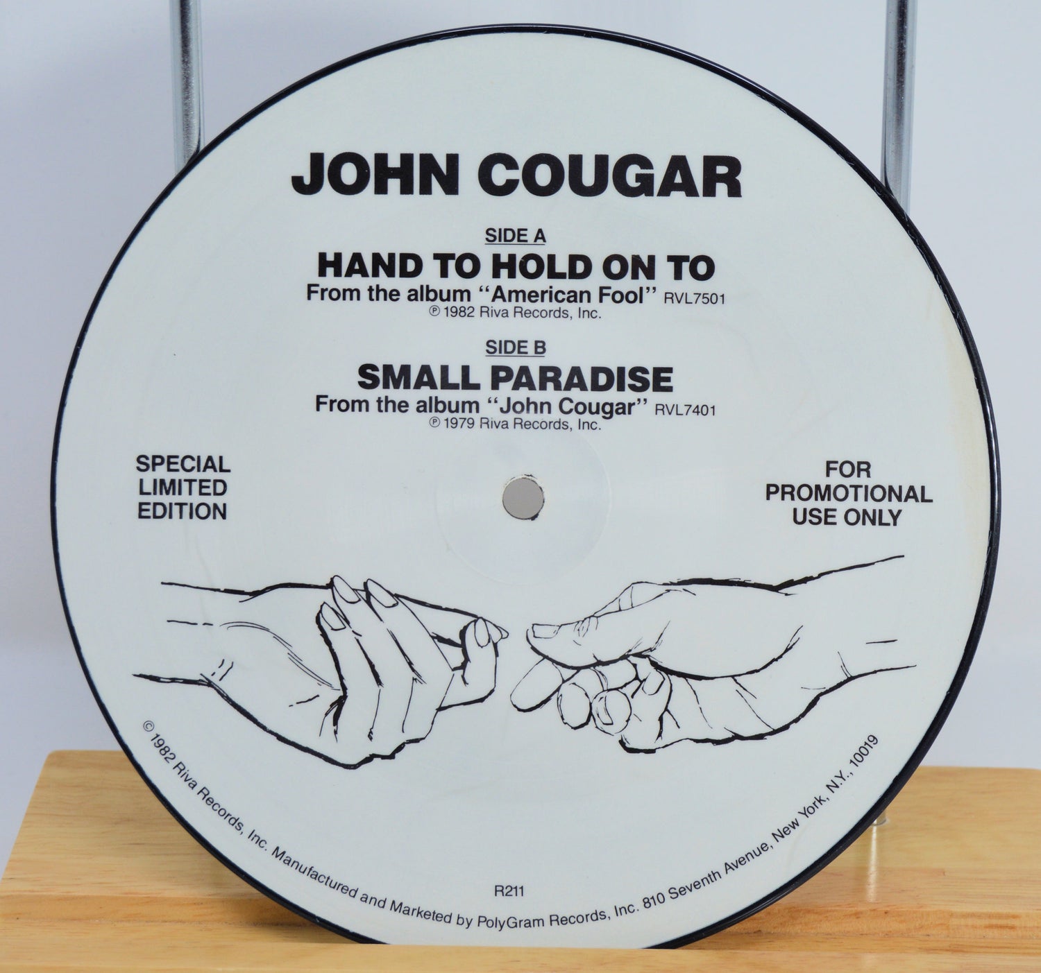 Vinyl record label with 'John Cougar' text and hand illustration on a wooden surface.
