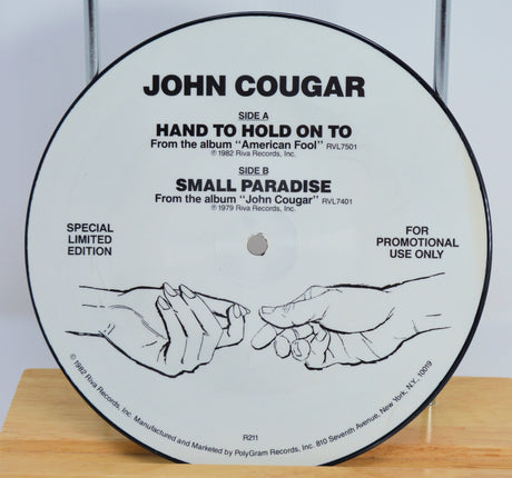 Vinyl record label with 'John Cougar' text and hand illustration on a wooden surface.