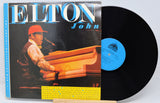 Vinyl record with cover featuring Elton John playing piano, on a white background