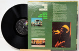 A vinyl record partially pulled from its sleeve, showing the black record on the left and the green album cover on the right. The cover features the text 'JOHN LEE HOOKER' and 'never get out of these blues alive,' along with printed photos and song listings.