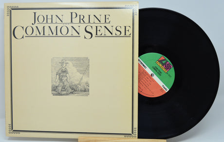 John Prine's 'Common Sense' vinyl record album, showing the beige illustrated cover sleeve alongside the black 12-inch record with a green and orange label.
