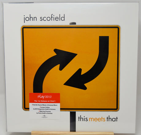 John Scofield's 'This Meets That' vinyl record cover, featuring a large yellow road sign with black arrows on the front of the white album packaging.
