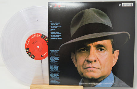 A Columbia Records vinyl record shown with its back cover standing upright and a translucent clear record partially pulled out on a small wooden stand. The cover features a large portrait of a man in a hat against a dark background, with tracklist text and a red Columbia label visible on the record.
