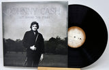 Johnny Cash 'Out Among the Stars' vinyl record album with the cover sleeve on the left and the black LP record partially visible on the right, displayed on a wooden stand against a light gray background.