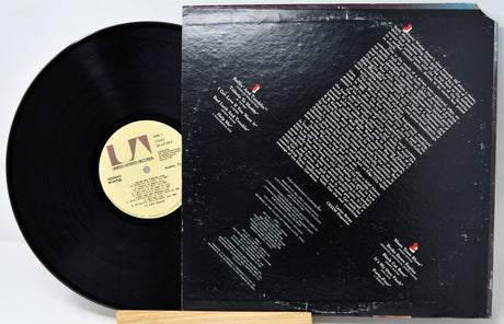 A black vinyl record partially pulled from its sleeve, showing the record label insert and the back cover with tracklist text, photographed on a white background.