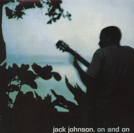 Silhouette of a person playing a guitar with a backdrop of tropical foliage and a body of water.