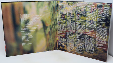 An open printed booklet or album-style book spread on a white surface, showing two printed pages with blurred forest imagery and dense text blocks. No person or real environment is present beyond the tabletop, so this is Product/Packaging rather than Lifestyle.