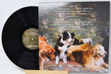 A vinyl record partially pulled from its jacket, showing the black record on the left and the back cover artwork on the right. The cover features a scenic landscape with several dogs, including a black-and-white dog in the center.