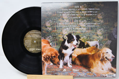 A vinyl record partially pulled from its jacket, showing the black record on the left and the back cover artwork on the right. The cover features a scenic landscape with several dogs, including a black-and-white dog in the center.