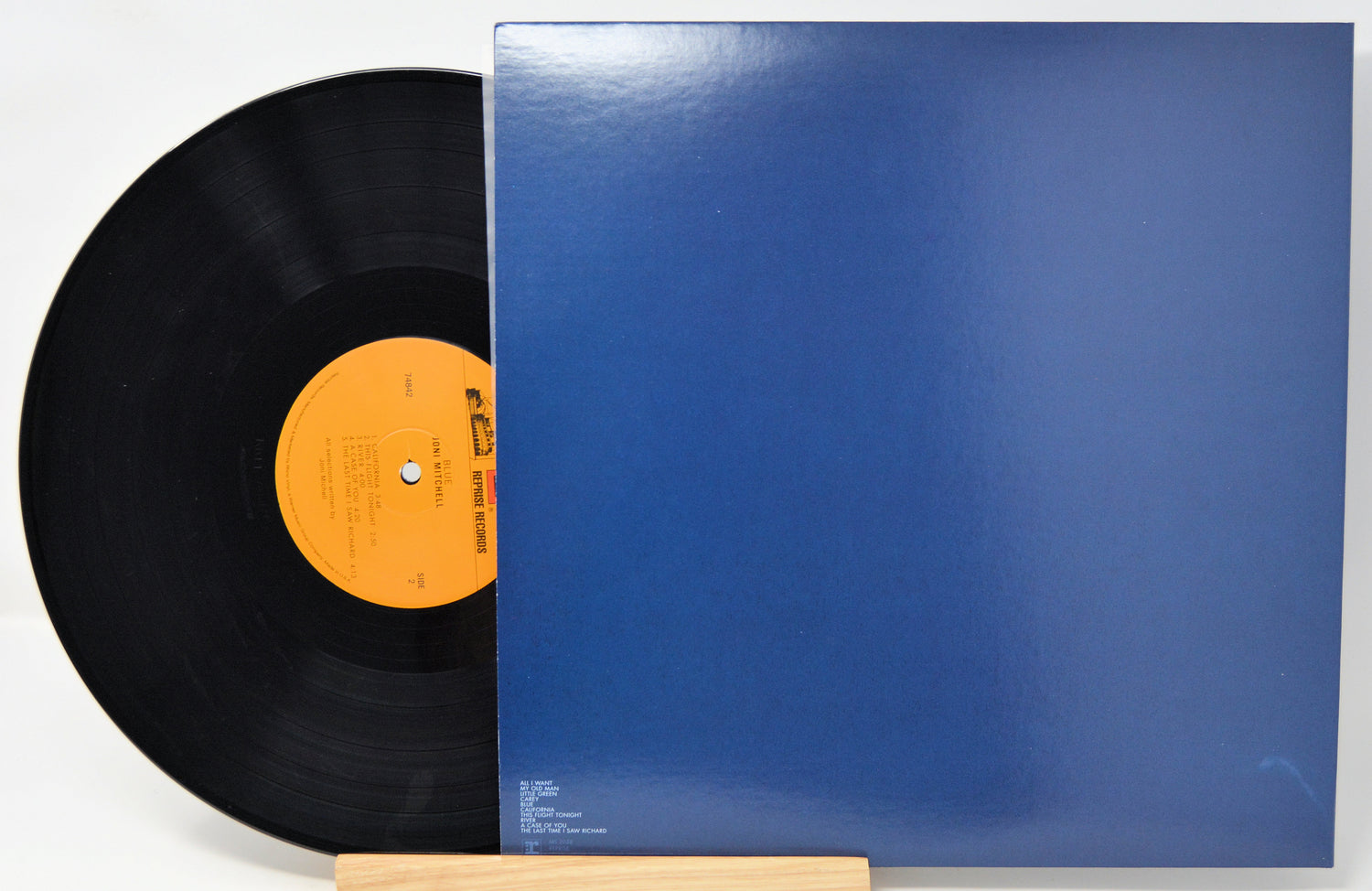 A vinyl record partially pulled from its blue sleeve, displayed on a small wooden stand against a white background.