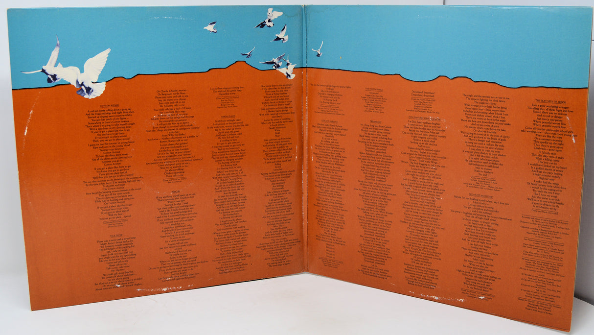 An open book or printed booklet spread open on a white surface, showing a large orange-brown field covered with many small black text entries, with a blue sky and white birds illustrated across the top.