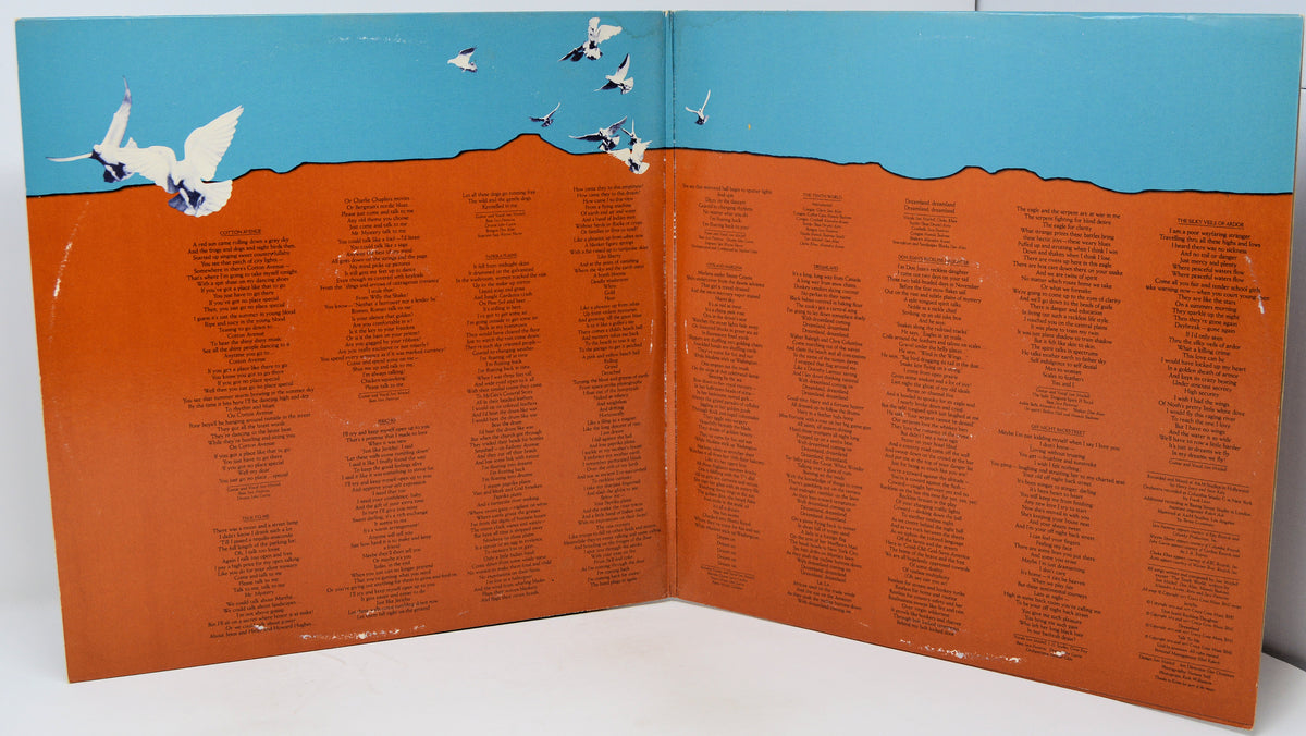 An open book or printed booklet spread open on a white surface, showing a large orange-brown field covered with many small black text entries, with a blue sky and white birds illustrated across the top.