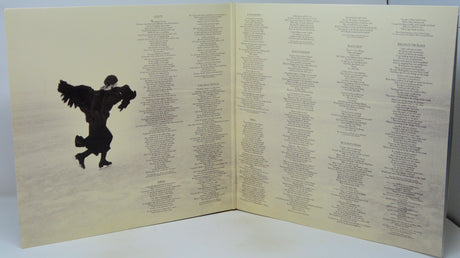 An open book or album cover spread showing a large black winged figure on a pale beige background, with dense columns of small text printed on both pages.