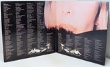 An open vinyl record sleeve or booklet showing printed track listings on both pages and a close-up photograph of a woman's face across the center, photographed against a plain light background.