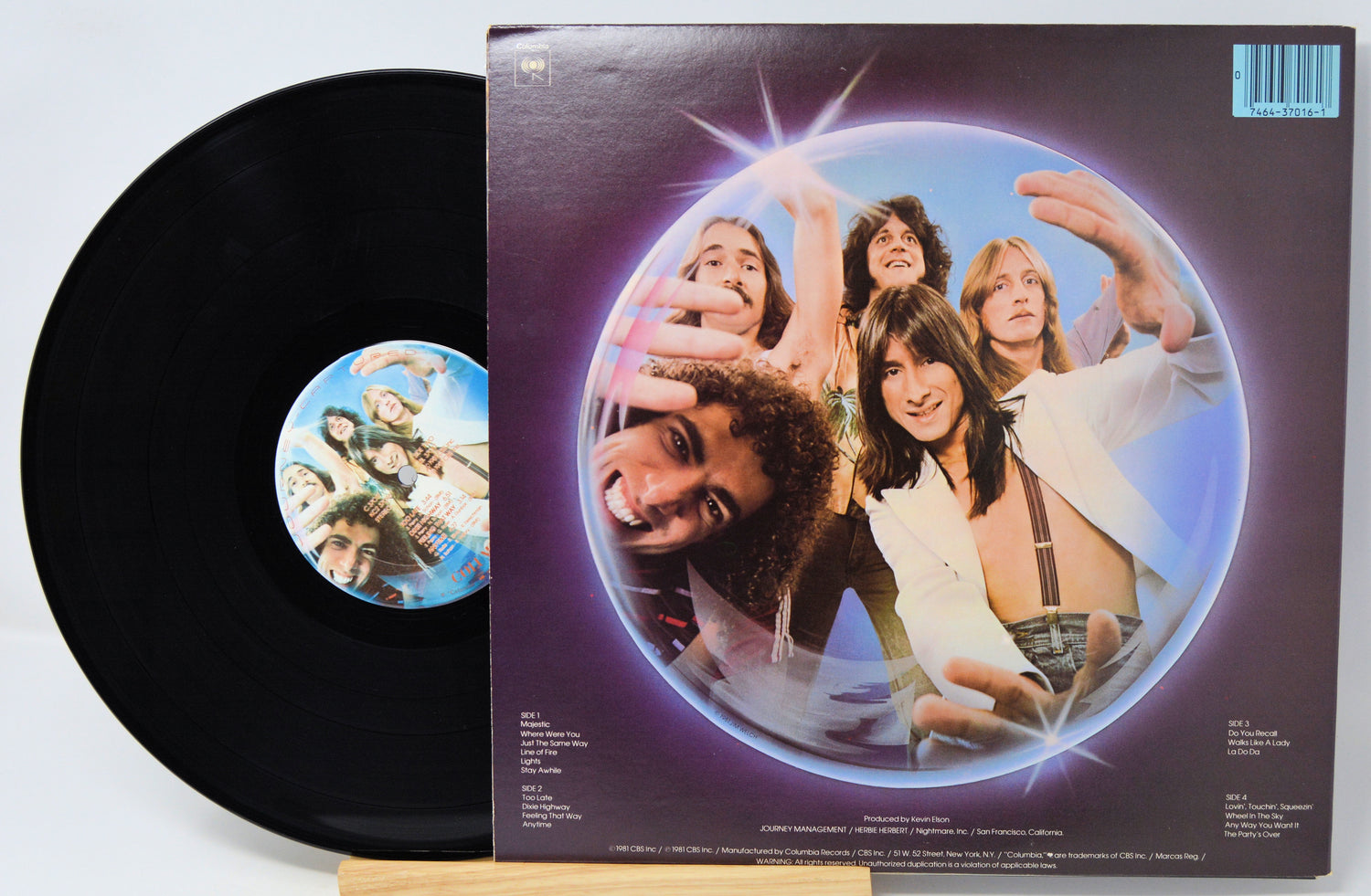 A vinyl record partially pulled from its sleeve, showing the black record and the back cover artwork with a circular photo of five people against a purple background.