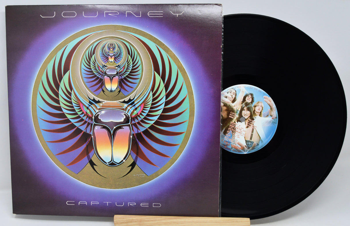 Journey 'Captured' vinyl record LP with the album cover sleeve and a black record partially pulled out, displayed on a small wooden stand against a light gray background.