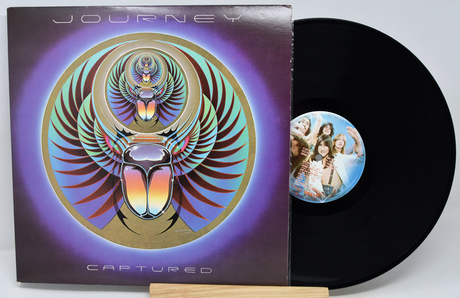 Journey 'Captured' vinyl record LP with the album cover sleeve and a black record partially pulled out, displayed on a small wooden stand against a light gray background.