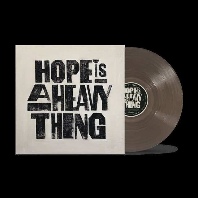 A vinyl record partially pulled from its sleeve, showing the album cover with the text 'HOPE IS A HEAVY THING' in large distressed black letters on an off-white background. The vinyl itself is a muted taupe-brown color, and the center label repeats the album title.