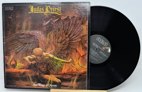Judas Priest 'Sad Wings of Destiny' vinyl record LP with the illustrated album cover sleeve and a black record partially visible, photographed against a light gray background.