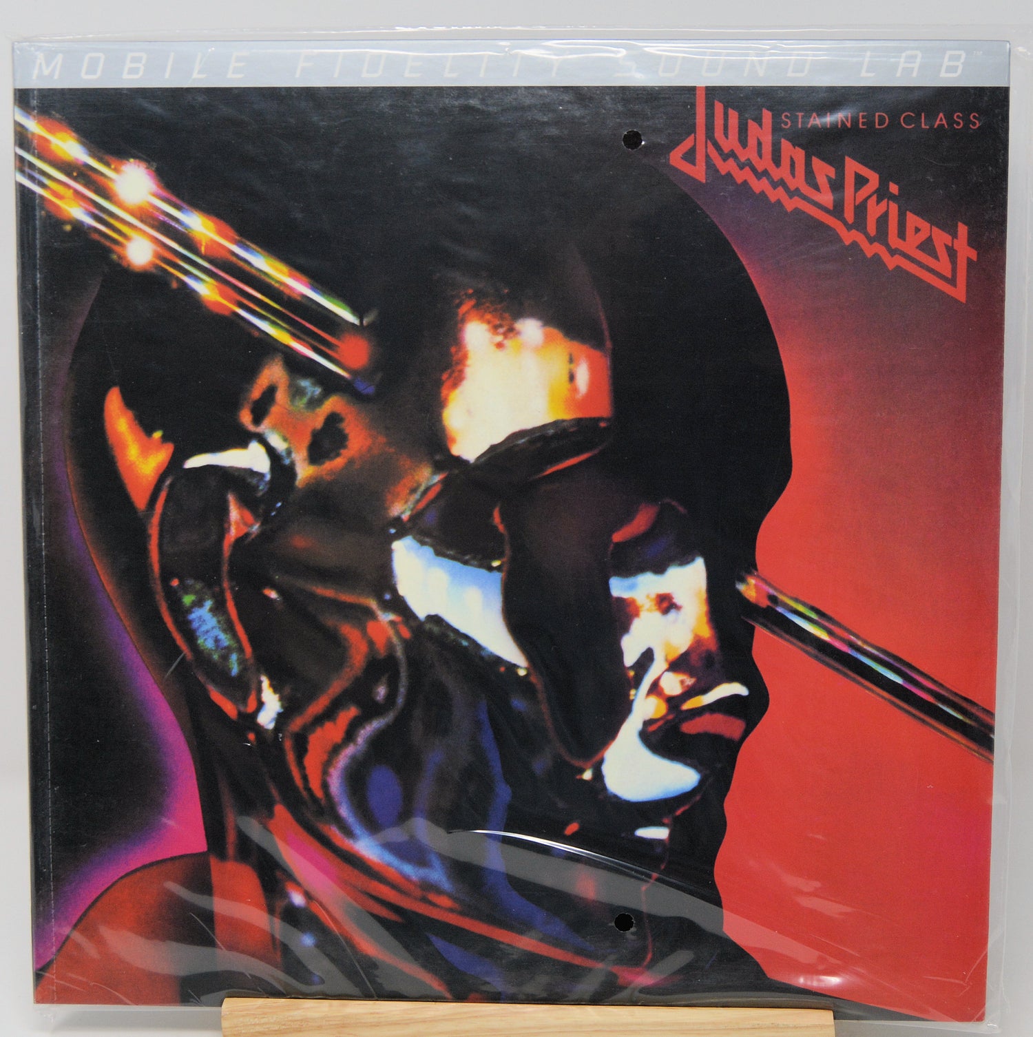 Judas Priest 'Stained Class' vinyl record cover in shrink wrap, featuring a stylized metallic face in black, red, orange, and blue tones.