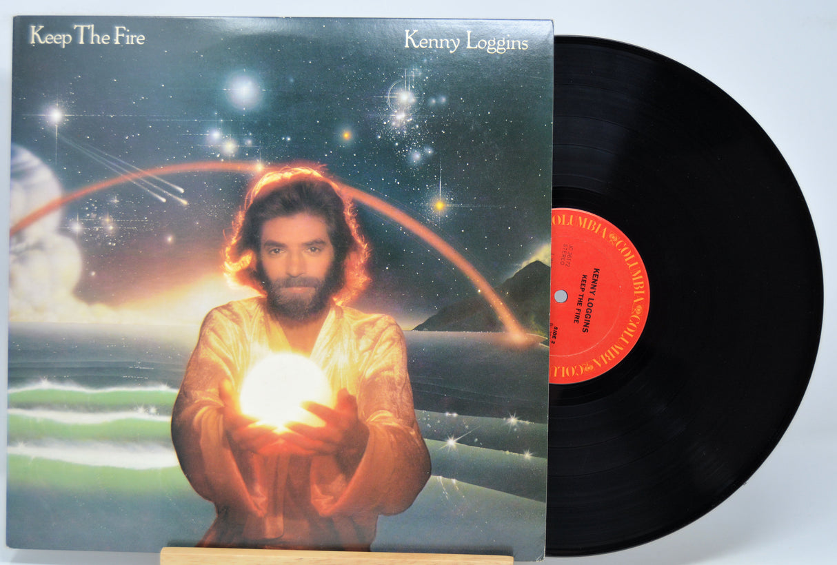 Vinyl record with cover featuring a person holding a light bulb against a cosmic background, titled 'Keep The Fire' by Kenny Loggins.